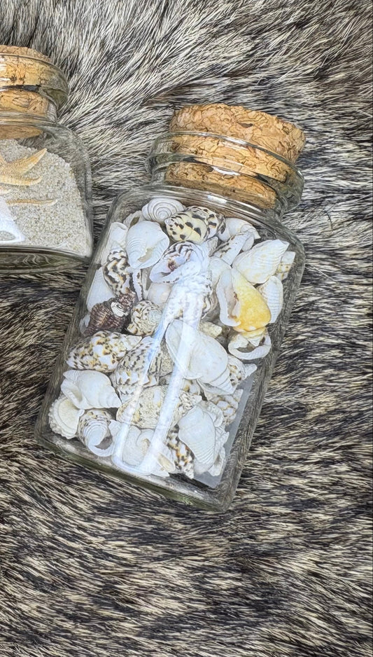 Three small glass bottles with cork lids containing various items on a fur surface